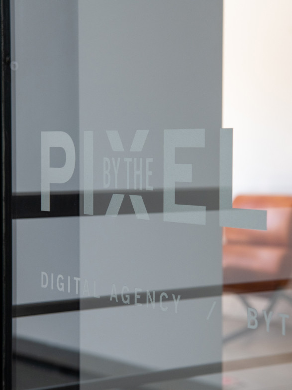 A glass door embossed with the By the Pixel logo